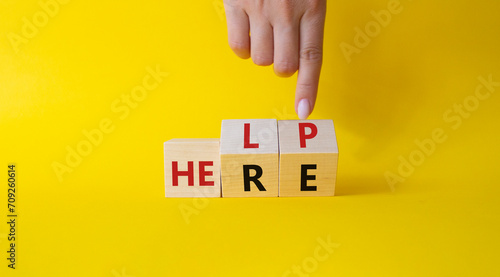 Help is here symbol. Businessman hand points at cube with words Here to Help. Beautiful yellow background. Business and Help is here concept. Copy space