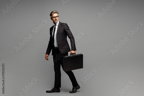 Full body side view adult employee business man corporate lawyer wears formal black suit shirt tie work in office hold in hand briefcase look aside isolated on plain grey background studio portrait.