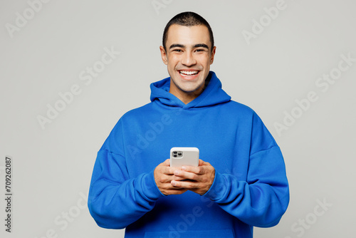 Foto Young smiling happy middle eastern man he wearing blue hoody casual clothes hold in hand use mobile cell phone look camera isolated on plain solid white background studio portrait