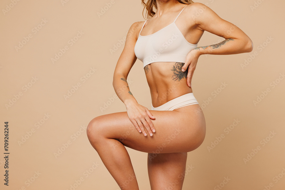 Close up cropped young nice lady woman with slim body perfect skin wear nude top bra lingerie stand put hand on thigh raise up leg isolated on plain pastel beige background Lifestyle diet fit concept - obrazy, fototapety, plakaty 