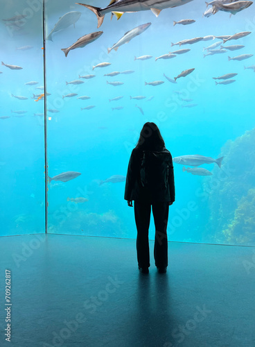 the girl stands in front of a large aquarium with fish. Oceanarium with sharks photo