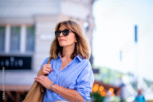 Close-up of a beautiful mid aged woman wearing sunglasses and walking on the street