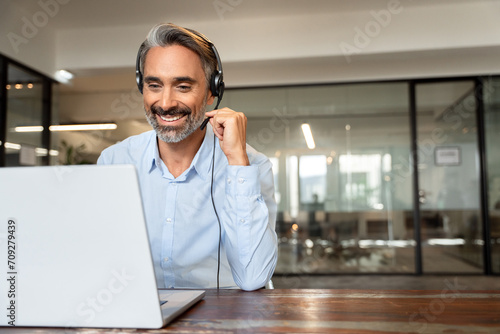 Happy senior latin Hispanic man in wearing headphones, helping as callcenter consult assistant. Smiling mature 40s years old mixed race businessman holding video call with clients partners. Copy space photo