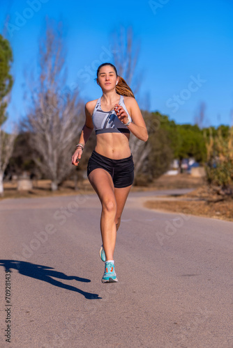 Beautiful young female runner girl, dressed in running shorts and white top, running suspended in the air looking at the horizon, happy and free on an asphalt road at sunrise in a mountain park.
