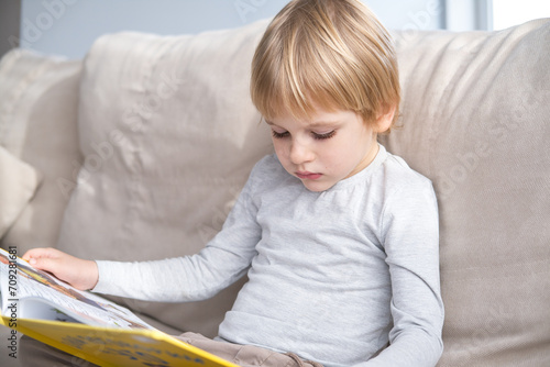 little boy reading book, sitting on sofa at home