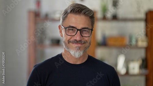 Portrait of happy, confident older man at home looking at camera smiling. Mature age, middle age, mid adult casual guy in 50s, bearded, gray hair, wearing glasses.