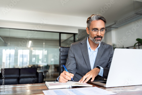 Middle-age Hispanic man using laptop computer for business studying, watch online virtual webinar training meeting, video call. Focused mature Indian or Latin businessman work in office, copy space.