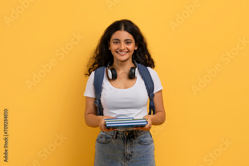 Happy cute young indian woman student posing on yellow background photo