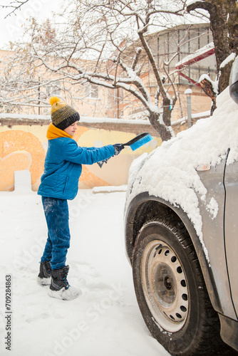 Cute little boy is helping his father brush the snow from the car. Snow removal from the car concept of car care during