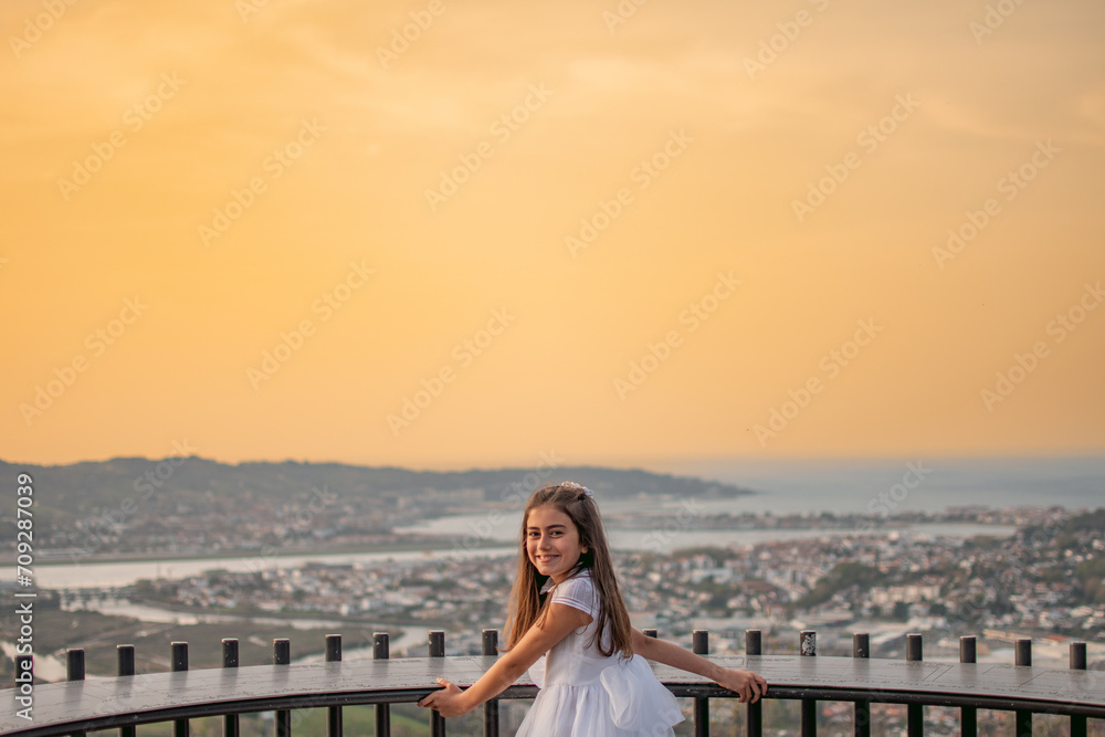Girl in a first communion dress celebrating her day on a viewpoint with the city and the bay in the background during sunset