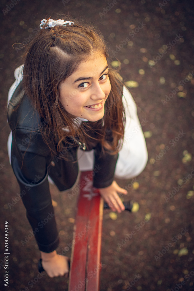 Fototapeta premium Little girl in communion dress and black leather jacket playing on a swing in a public park