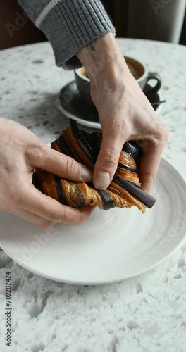 Close-up of tearing a freshly baked chocolate croissant in a bakery, cup of black coffee in the background
