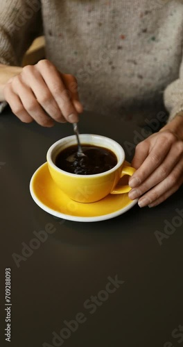 Unrecognizable caucasian woman in a cozy sweater drinking a cup of hot black coffee, sitting at the table