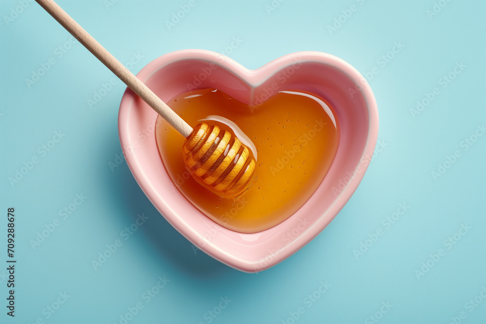 Honey and dipper in a pastel pink heart shaped bowl on blue surface. Honey and dipper in a pastel pink heart shaped bowl on blue surface.