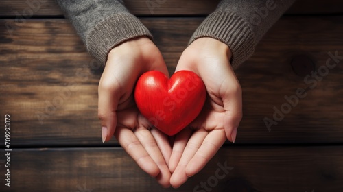 Close-up of a woman s hands holding a red heart on a wooden background. Valentine s Day greeting card. A symbol of love. View from above.