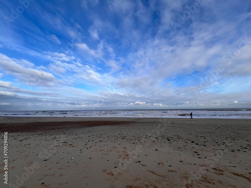 Beautiful landscape of sandy beach at Winterton on Sea in Norfolk East Anglia uk vast ocean view big cloudy blue grey skies over the water reflect sky clouds person walking in wild natural environment