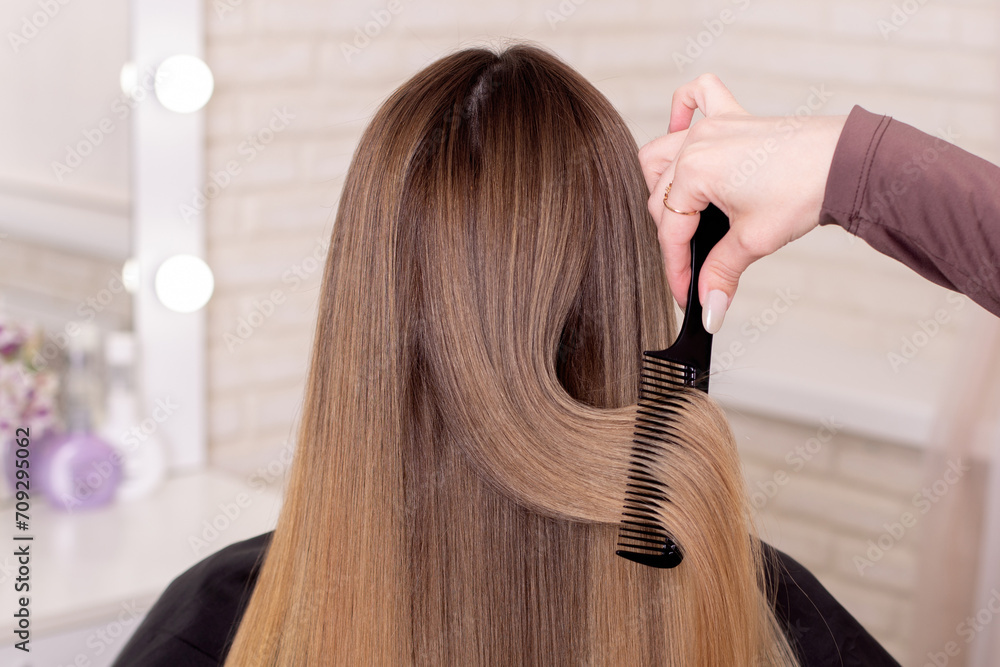 Fototapeta premium Hairdresser's hand brushing long natural blonde hair in beauty salon