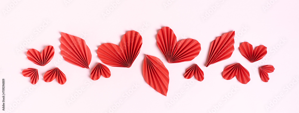 Web banner made of red curly hearts and leaves on a pink background top view