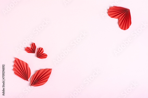 Composition of folded red paper hearts and leaves on a pink background top view copy space