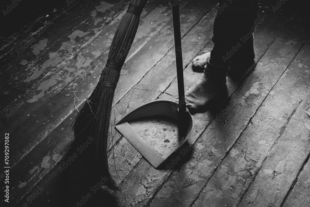 Women's feet on the floor and a broom and dustpan nearby, a girl sweeping the floor of the house, black and white photo