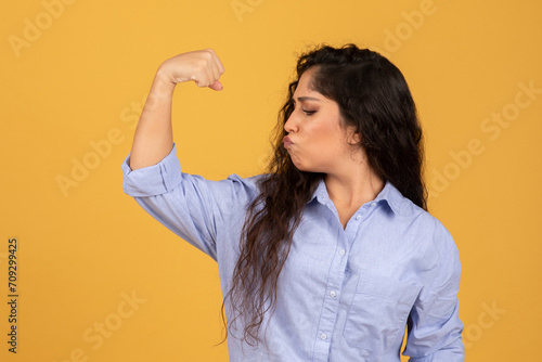 Confident young woman with long dark hair flexing her bicep and puckering her lips