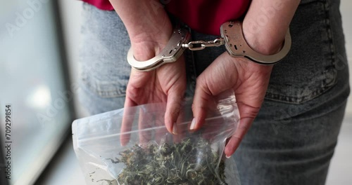 Woman in handcuffs holds pack of dry marijuana behind back photo