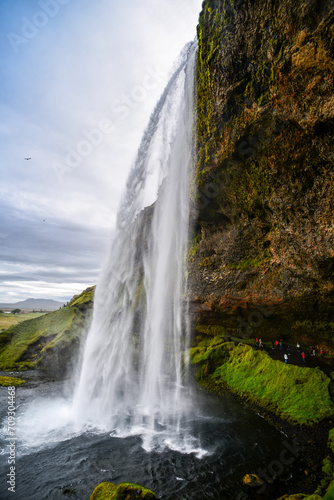 Tourists walking under the popular Seljalandsfoss waterfall, southern Iceland.