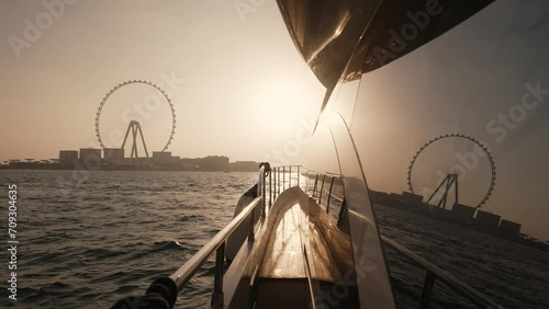 Luxury yacht sailing in Dubai Marina, Ferris wheel slow motion view during sunset photo