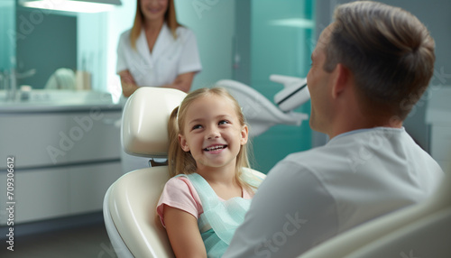 A child sitting in a dental clinic chair smiles at a dentist before undergoing a oral inspection