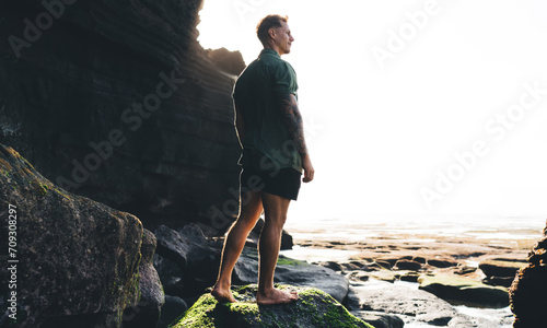 Man standing on rocky terrain by cliff on sunny day