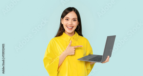 Positive young brunette woman holding and using laptop