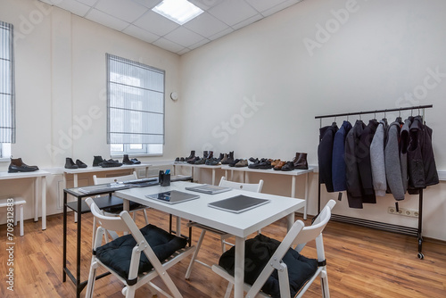 A showroom with a table for visitors, clothes on a hanger and shoes on the shelves. © alhim