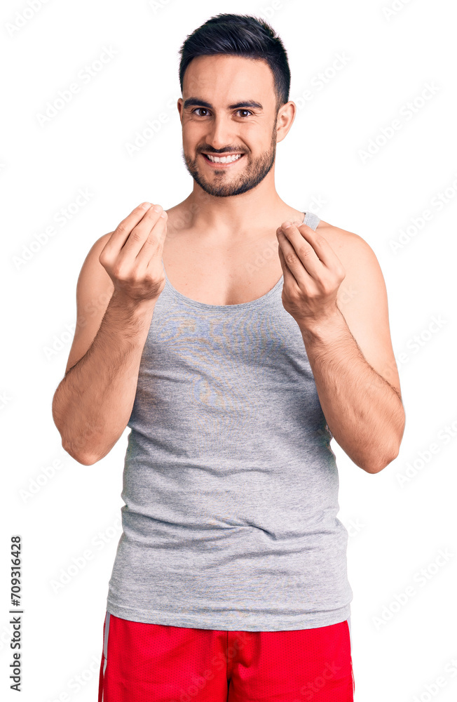 Young handsome man wearing swimwear and sleeveless t-shirt doing money gesture with hands, asking for salary payment, millionaire business Young handsome man wearing swimwear and sleeveless t-shirt doing money gesture with hands, asking for salary payment, millionaire business