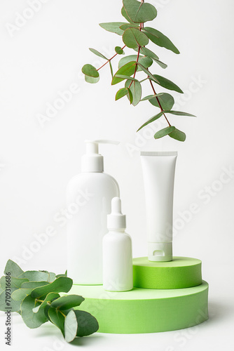 Set of organic skin care products in white unbranded containers on green cosmetic podium with aromatic eucalyptus leaves close up. Cosmetic branding concept. Vertical image.