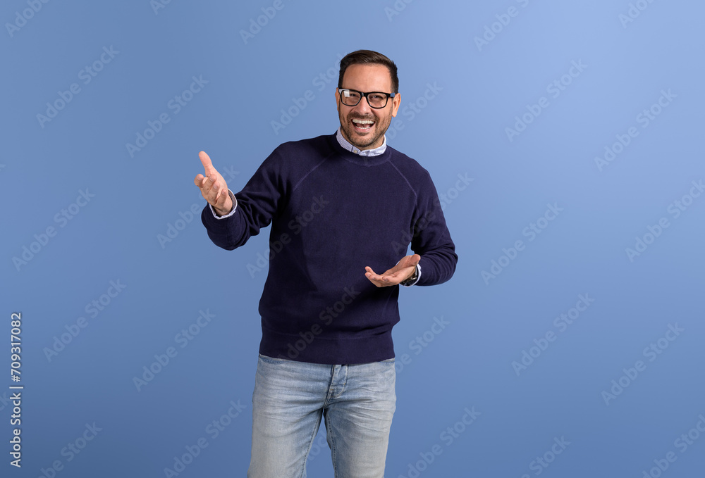 Fototapeta premium Portrait of handsome businessman in eyeglasses gesturing and laughing at camera on blue background