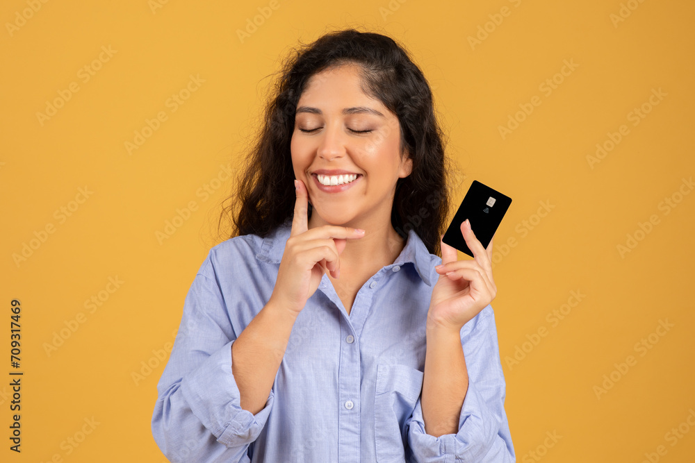 A delighted young woman with curly hair playfully holds a credit card A delighted young woman with curly hair playfully holds a credit card