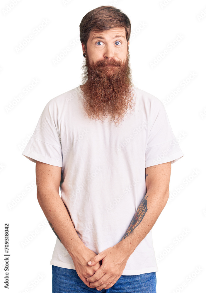 Handsome young red head man with long beard wearing casual white tshirt puffing cheeks with funny face. mouth inflated with air, crazy expression. Handsome young red head man with long beard wearing casual white tshirt puffing cheeks with funny face. mouth inflated with air, crazy expression.