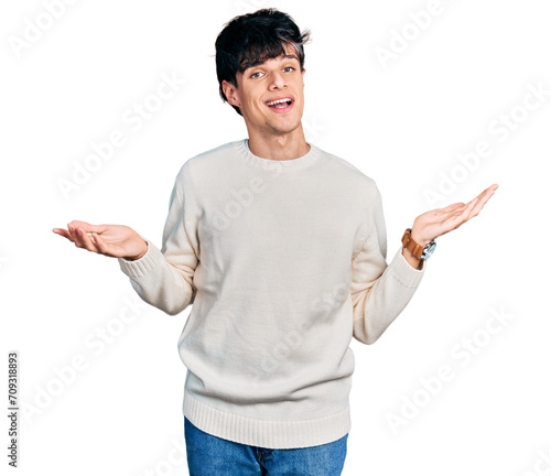 Handsome hipster young man wearing casual winter sweater clueless and confused expression with arms and hands raised. doubt concept.