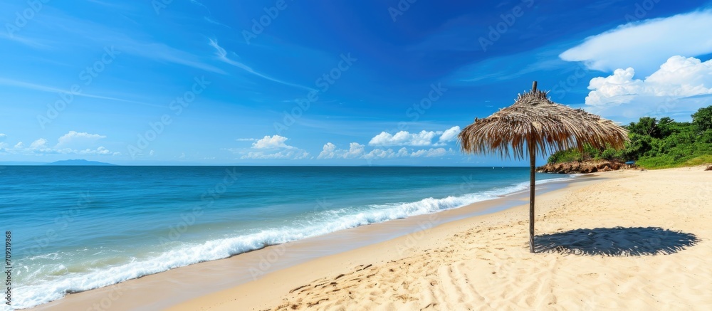A peaceful beach with a straw umbrella on golden sand by the sea, complimented by clear skies and calm waters for a serene beach escape. - obrazy, fototapety, plakaty 