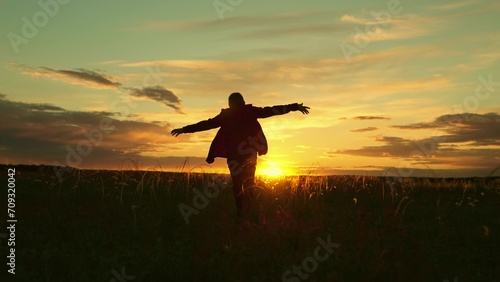Child aviator runs across field, child dreams of becoming an airplane pilot. Happy child runs with arms raised like airplane wings, childhood dream in park. Silhouette of boy running at sunset