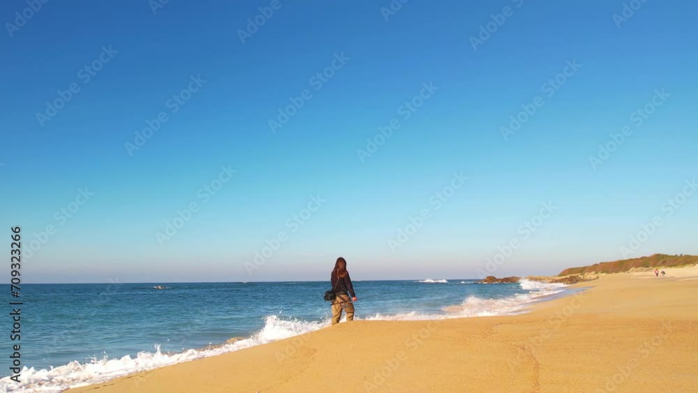 Fisherwoman walking on a beach, near the sea, with her fishing tackle Fisherwoman walking on a beach, near the sea, with her fishing tackle