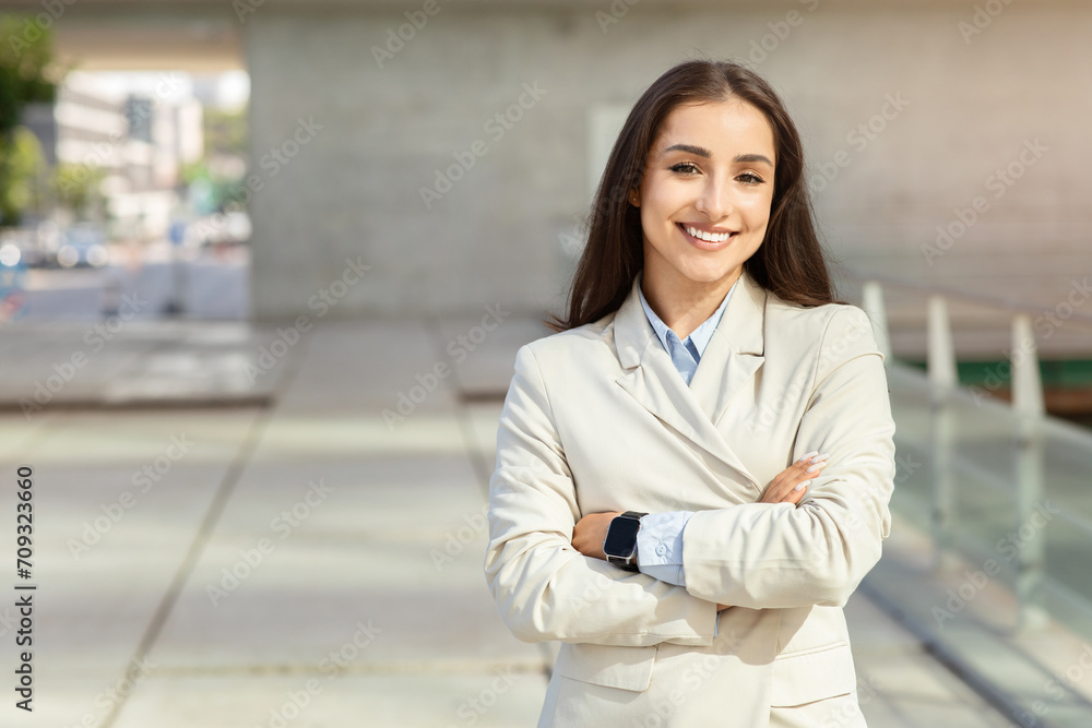 Smiling young professional woman confidently standing with arms crossed, wearing a smart business suit Smiling young professional woman confidently standing with arms crossed, wearing a smart business suit