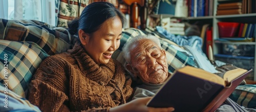 Asian woman reading book to elderly man in bed.