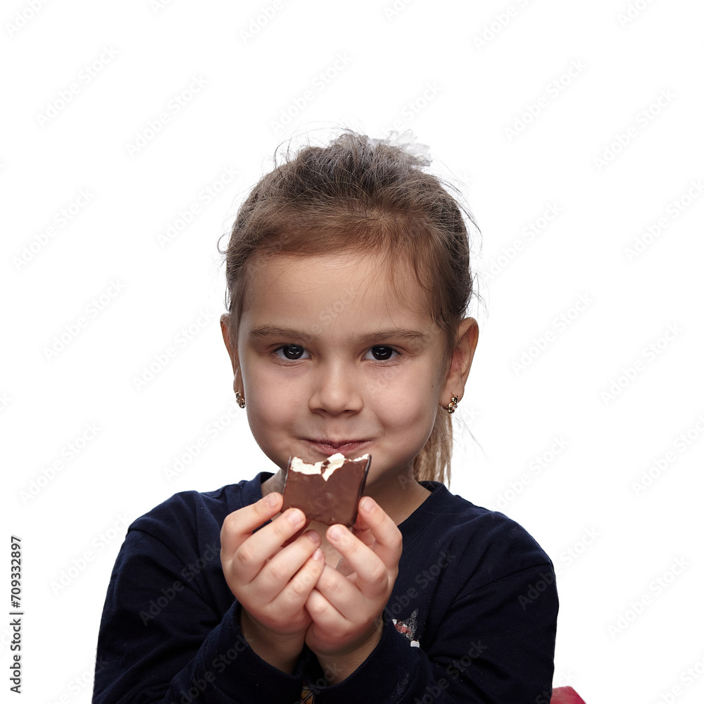 Cute little girl with a chocolate candy in her hands, eating and smiling