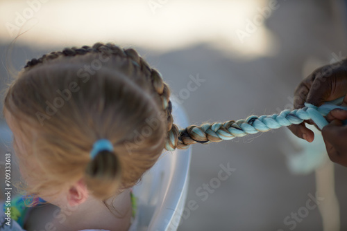 holding braids with pink color on little kid head. stylist applying braiding hair on young baby. photo