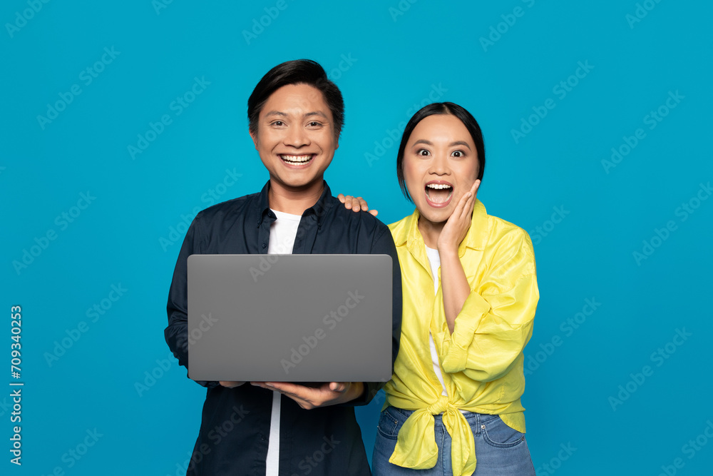 Surprised and happy Asian couple with a laptop, the woman touching her face in excitement Surprised and happy Asian couple with a laptop, the woman touching her face in excitement