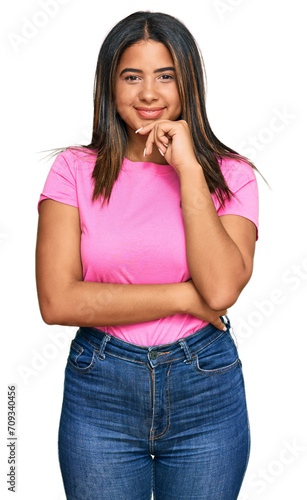 Young latin girl wearing casual clothes looking confident at the camera with smile with crossed arms and hand raised on chin. thinking positive.