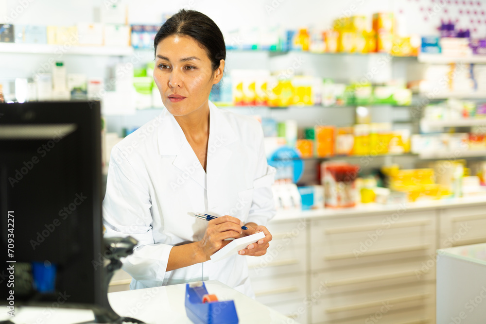 Female doctor or pharmacist working in pharmacy, using computer screen