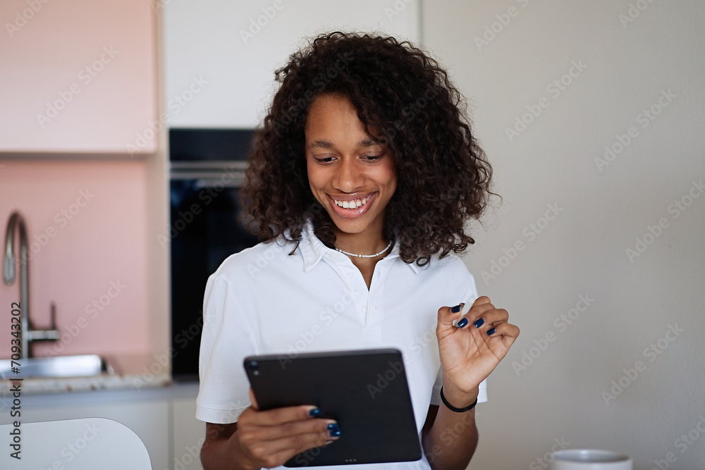 Beautiful young woman sitting at the kitchen counter, drinking coffee and using a tablet while relaxing at home in the morning. Working with a computer in the office at home Beautiful young woman sitting at the kitchen counter, drinking coffee and using a tablet while relaxing at home in the morning. Working with a computer in the office at home