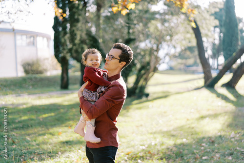 Dad with a smiling little girl in his arms stands in the autumn park